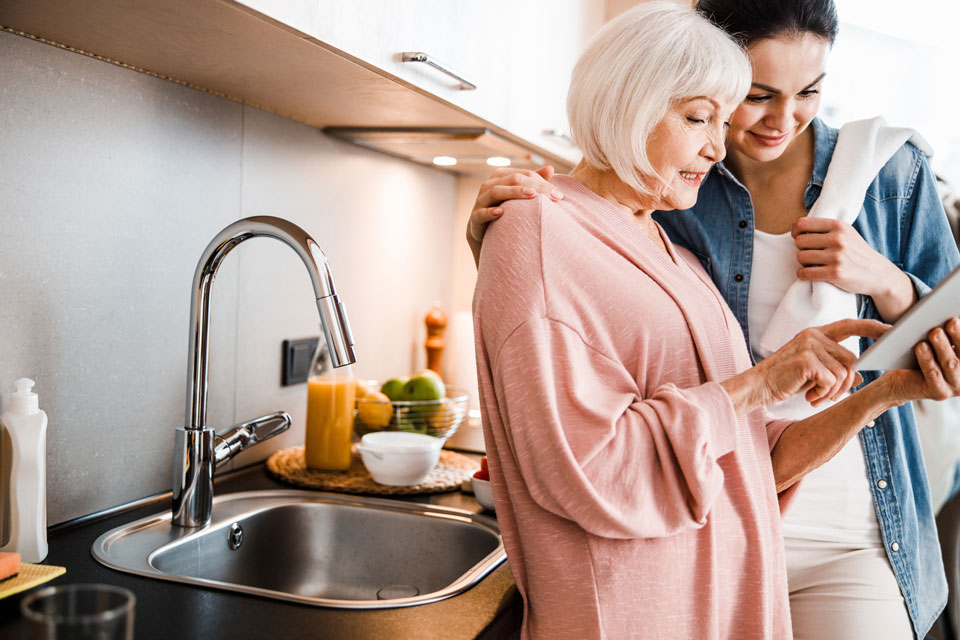 A grandmother and her daughter looking at a tablet while standing next to the sink